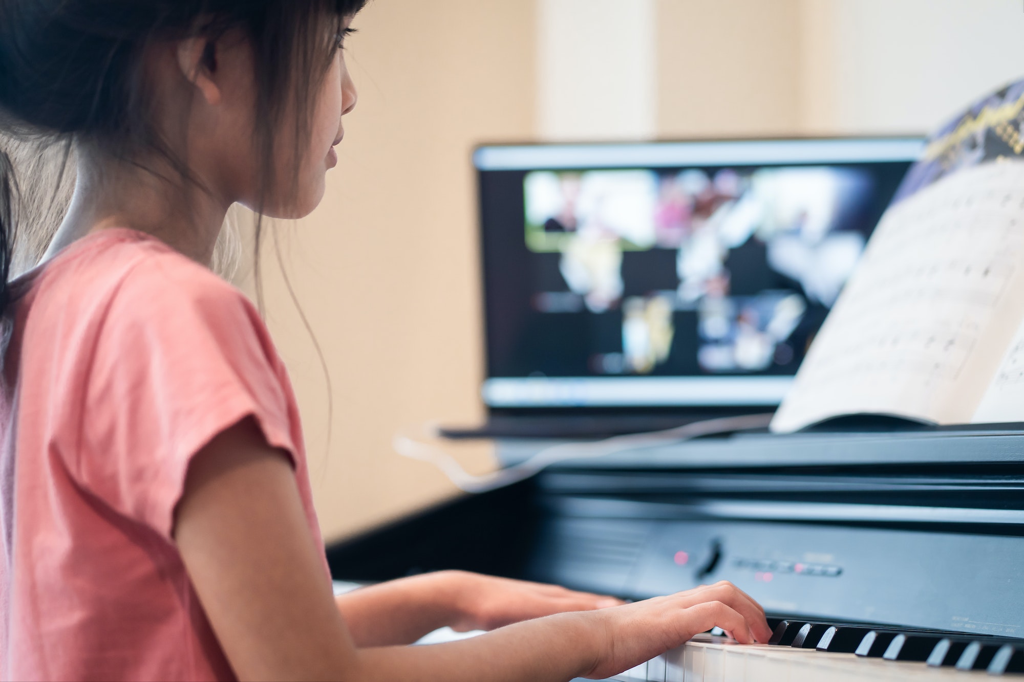 asian little girl learning piano from computer connecting to internet music online class by school
